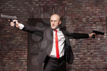 Serious contract killer shooting action wallpaper, background or poster. Bald assassin in red tie fires a pistols with two hands on city street. 
Professional special agent on secret mission