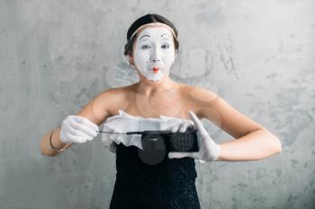 Mime female artist performing with mobile phone. Woman circus clown. Pantomime theater comedian with white makeup mask on face