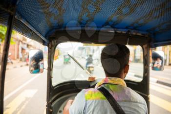 Tuk-tuk driver on road of Sri Lanka, view from car. Ceylon traditional tourist transport, local taxi