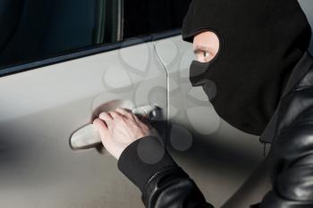 Carjacking danger, car insurance advertising concept. Male thief with balaclava on his head trying to open car door. Carjacker unlock vehicle