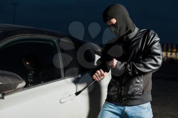 Male car thief hands trying to open door with jemmy. Carjacker unlock vehicle with crowbar on parking. Carjacking danger. Auto robbery vandalism