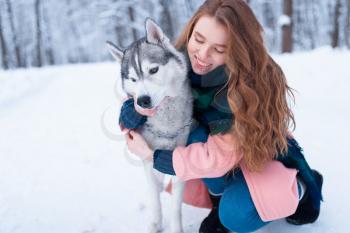 Pretty woman hugs with siberian husky, snowy forest on background. Cute girl with charming dog. Real friendship with pet