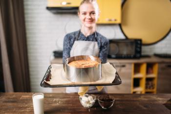 Woman cook in apron holds pan with fresh cake. Kitchen on background. Homemade dessert