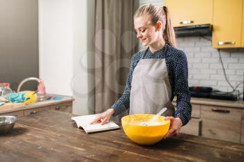 Young woman in apron reading the recipe of the cake. Sweet dessert cooking preparation. Kitchen on background