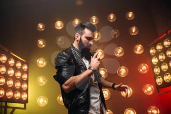 Brutal bearded singer with microphone sing a song on the stage with the decorations of lights