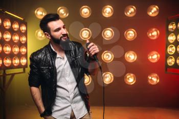 Brutal bearded singer with microphone on the stage with the decorations of lights