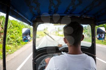Tuk tuk driver on road of Sri Lanka, view from car. Ceylon traditional tourist transport, local taxi