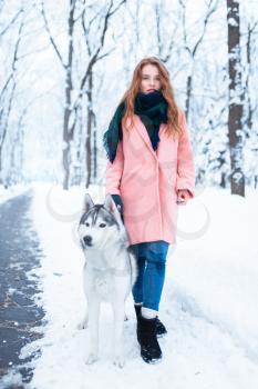 Portrait of young woman with husky dog, snowy forest on background. Cute girl walks in winter park with charming dog