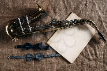 Saxophone, notes and bowtie on grunge canvas background, closeup view. Brass band instrument concept. Classical sax, jazz music