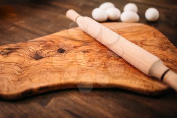 Cutting board, rolling pin and eggs on wooden background closeup view. Homemade food cooking concept. Dough baking