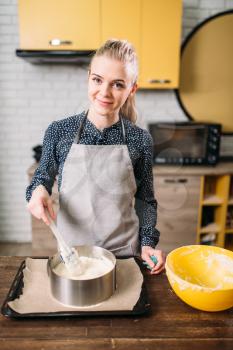 Woman cook in apron prepares cake ingredients in the pan with parchment paper. Kitchen on background