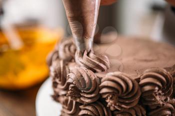 Decoration of chocolate cake with culinary syringe closeup view. Homemade dessert