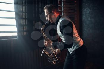 Male saxophonist playing jazz melody on saxophone against the window