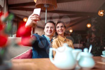 Love couple hugs and makes selfie on phone camera in restaurant. Man and woman happy together
