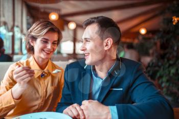 Young woman feeding man with a spoon in restaurant. Love cople at romantic dinner