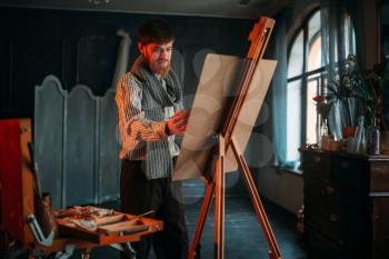 Male painter with brush in hand in front of easel. Oil paint, paintbrush drawing