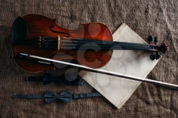 Violin, fiddlestick, notes and bowties on grunge sack texture, closeup view