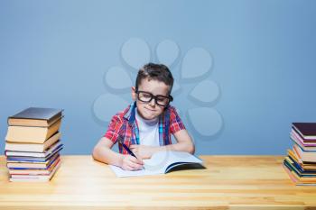 Young schoolboy learns homework, education concept. Pupil in glasses doing exercise in notebook