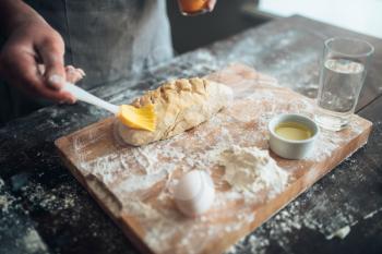 Baker hands smears butter on bread dough. Bread preparation on cutting board. Homemade fresh bakery