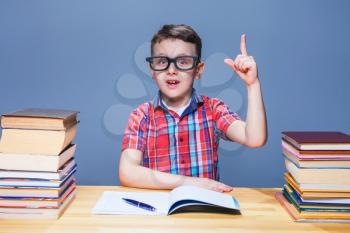 Little schoolboy learns homework at the desk in classroom. Pupil in glasses gets knowledge