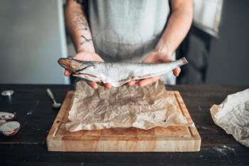 Male chef hands holds raw fish over wooden cutting board. Seafood cooking. Fresh sea food