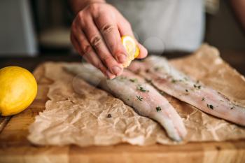 Male chef hands squeeze lemon on raw fish over wooden cutting board covered with parchment paper closeup view. Seafood cooking. Fresh sea food