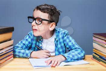 Pupil in glasses squints, bad vision concept. Young schoolboy sitting at the desk against many books