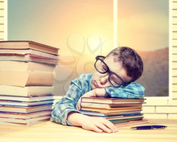 Little boy fells asleep over a stack of books in school library. Young schoolboy sleep at the desk against many books