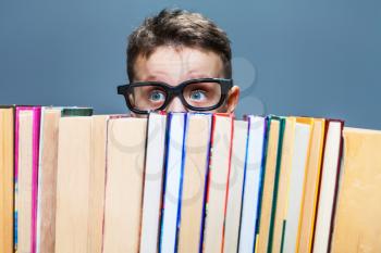 Little schoolboy in glasses peeking from behind the books. Education concept