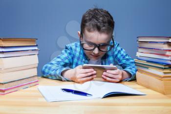 Young pupil in glasses playing on his phone in classroom. Little schoolboy with tablet pc