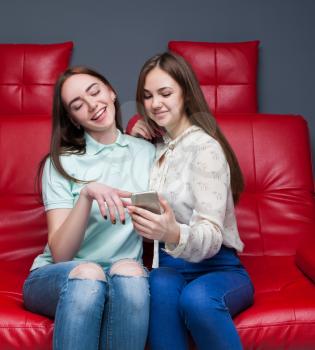 Portrait of two attractive girlfriends secretive on red leather couch