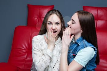 Two pretty girls gossiping on red leather couch. Women secrets