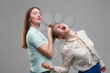 Two girls fighting, women quarrel, studio photo shoot. Girlfriends drag each other for hair