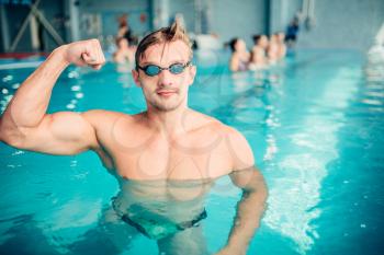 Athletic swimmer shows muscles, indoor swimming pool. Aqua sports exercise