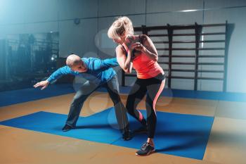 Woman in actoin on self-defense training with personal instructor, fighting workout in gym, martial art