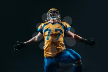 American football player in uniform and helmet on black background. Contact sport
