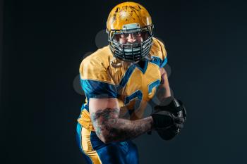 American football player in uniform and helmet, ball in hands, black background. Contact sport