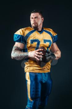 American football player poses with ball in hands, black background. Contact sport, national league