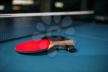 Red and black tennis rackets on the table against net, game concept. Ping pong sport equipment