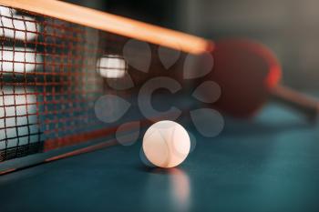 Ping pong ball on the table against net, selective focus, racket on background, game concept. Tennis sport equipment