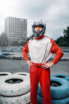 Kart driver with helmet in hands, karting track on background. Go-kart