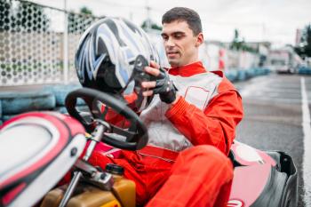 Go kart driver with helmet in hands on karting speed track. Go-kart motor sport
