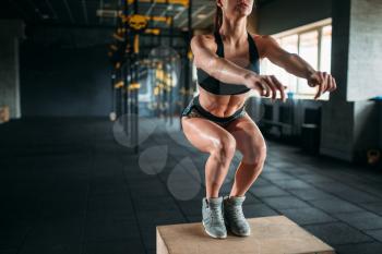 Young woman doing box jump exercise in fitness club. Attractive female athlete workout in gym