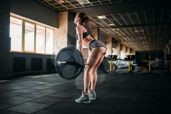 Muscular female athlete training with barbell in sport gym. Woman exercise with weight in fitness club