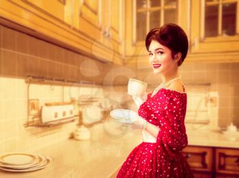 Attractive pinup girl with make-up drinks coffee on the kitchen cafe, 50 american fashion. Red dress with polka dots, vintage style