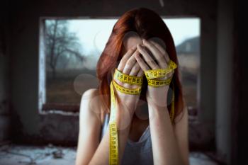 Woman covers face with her hands tied with measuring tape. Fat or calories burning concept. Weight loss