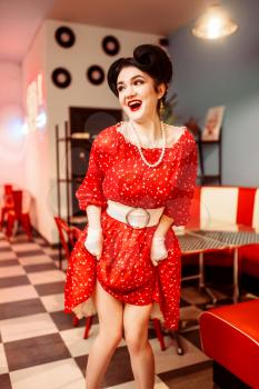 Pinup woman in red dress with white polka dots, vintage style. Retro cafe interior with checkerboard floor