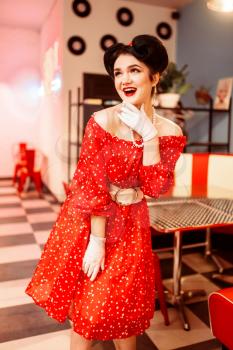 Pretty pin-up woman with make-up, red dress with white polka dots, vintage style. Retro cafe interior with checkerboard floor