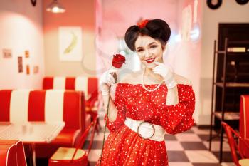 Sexy pin up woman with make-up holds red rose, dress with polka dots, vintage style. Retro cafe interior with checkerboard  floor