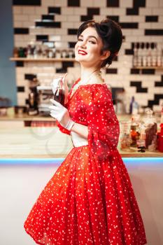 Pin up girl with make-up drinking popular carbonated drink, 50 american fashion. Red dress with polka dots, vintage style